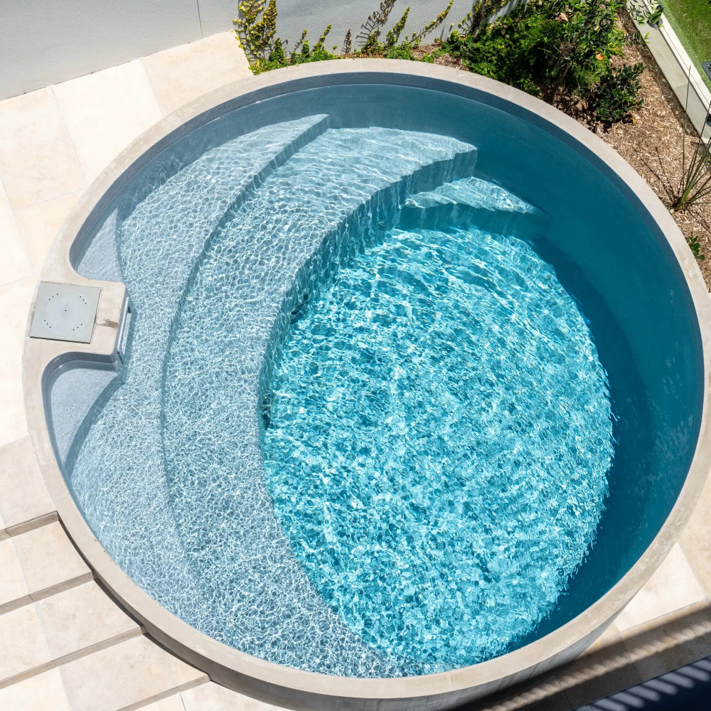 Circular pool with clear blue water, surrounded by a paved area.